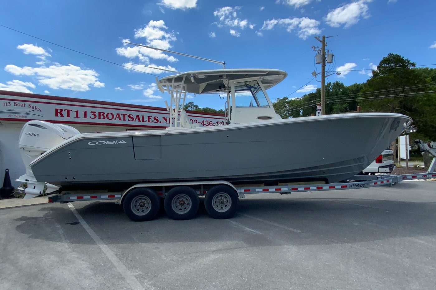 2027 Cobia 320 Center Console boat on trailer at dealership under blue sky.
