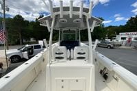 2027 Cobia 320 Center Console boat with T-top, docked near vehicles and trees.