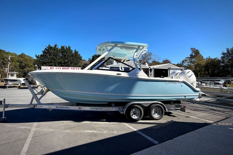 2027 Cobia 250 Dual Console boat on trailer at dealership under clear blue sky.