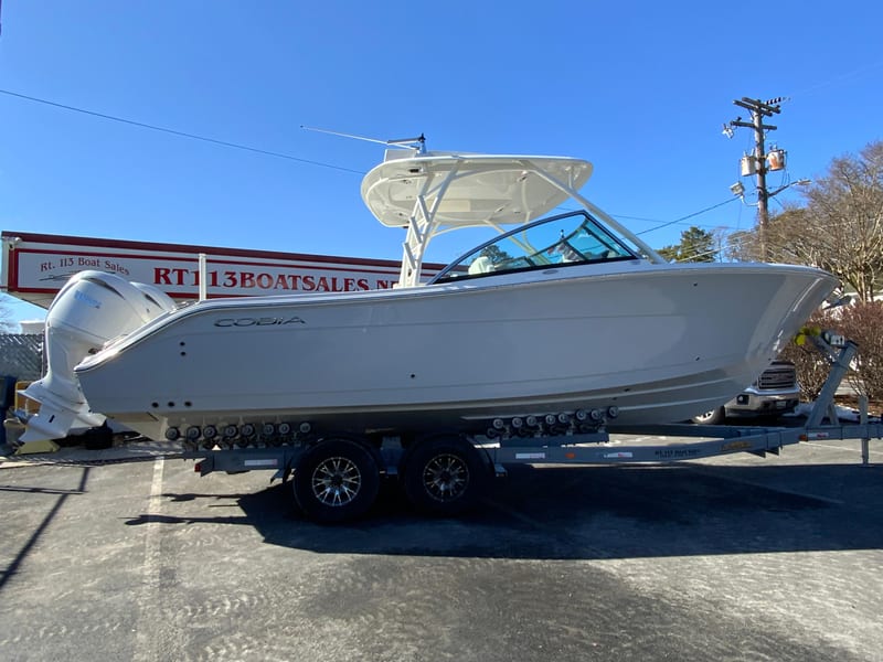 2025 Cobia 280 Dual Console boat on trailer at dealership under clear blue sky.