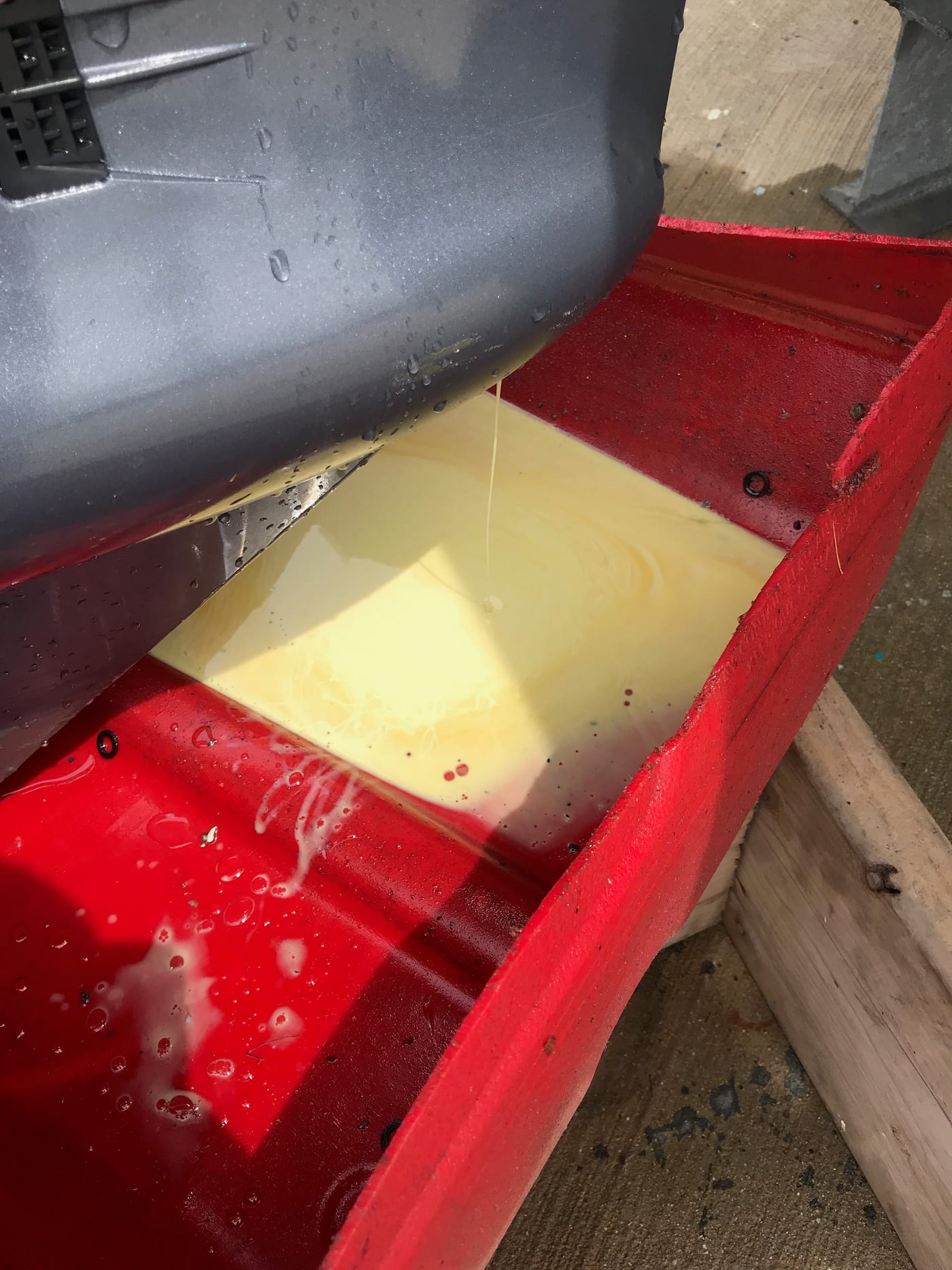 Gear oil drained from a Yamaha lower unit into a clear container, emulsified pale brown like coffee with cream instead of dark and clear